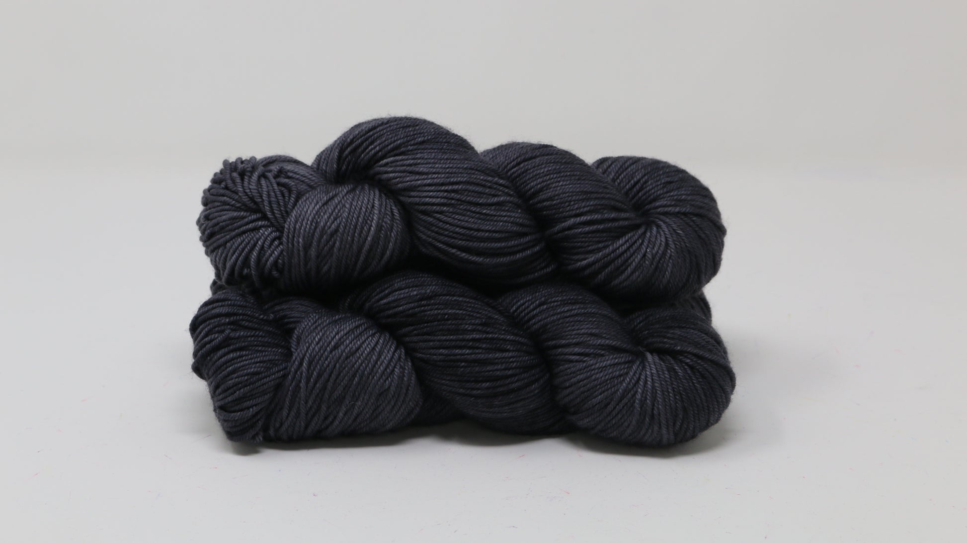 3 skeins of dark grey yarn on a white surface and background