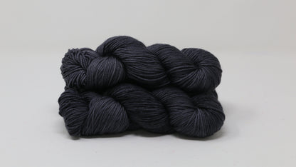 3 skeins of dark grey yarn on a white surface and background