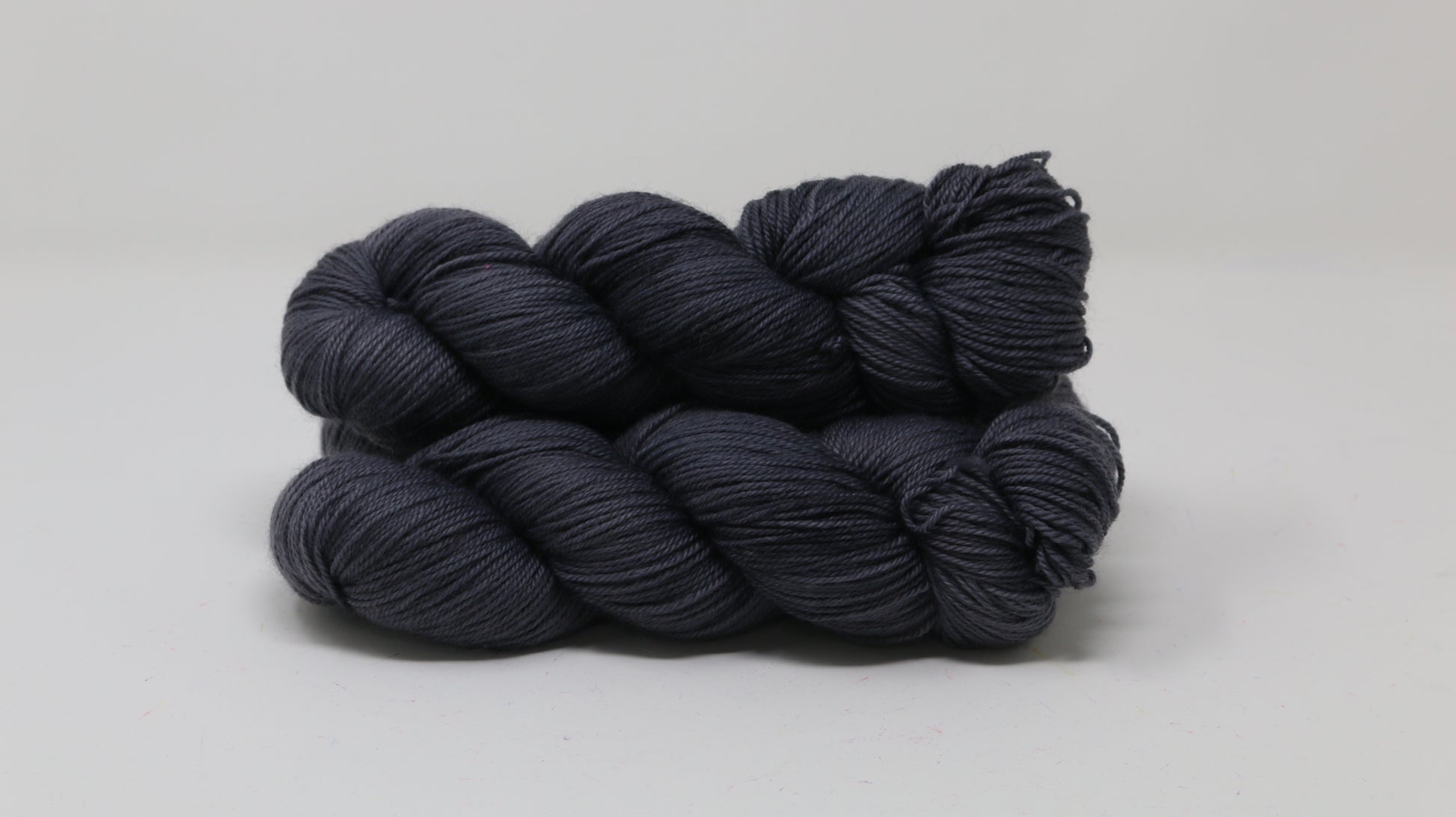 3 skeins of dark grey yarn on a white surface and background