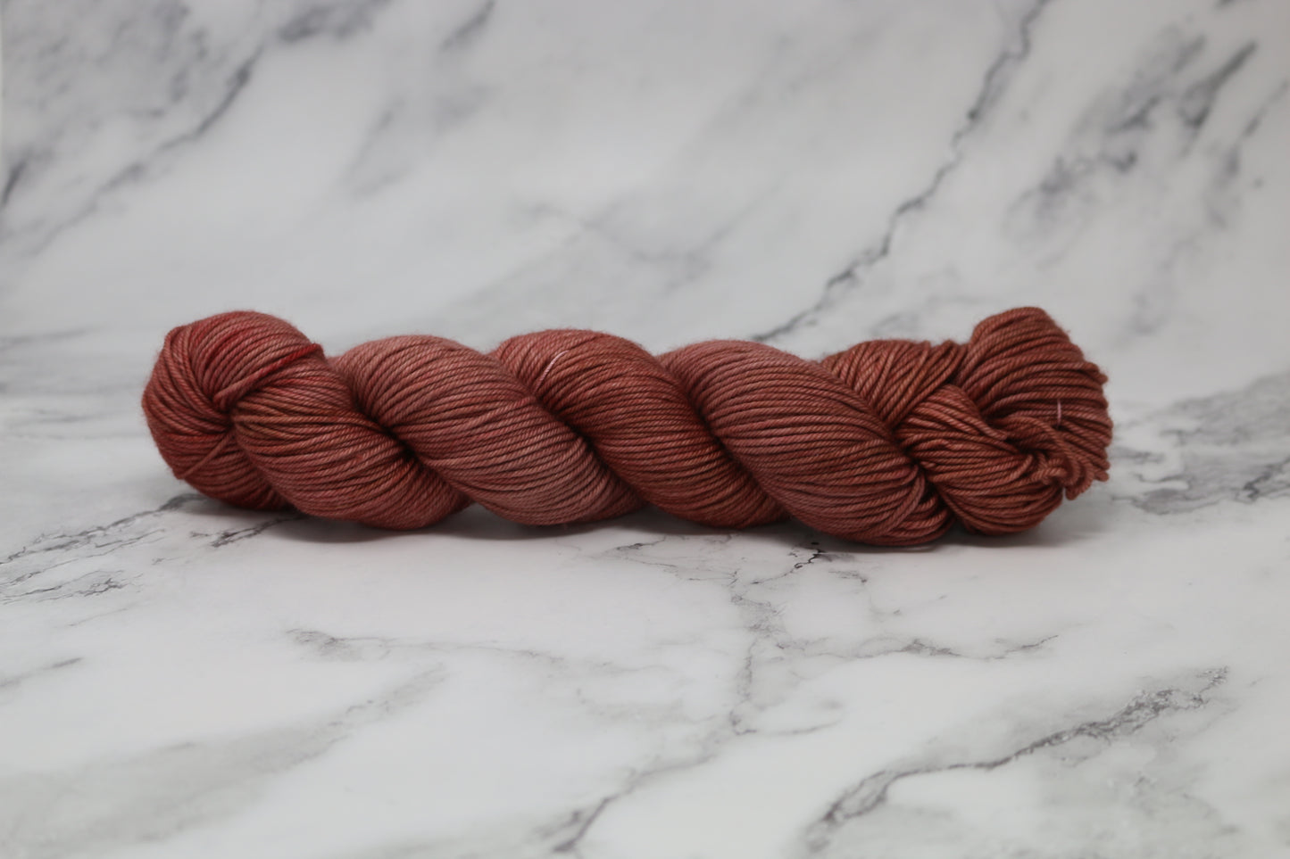 A skein of tonal red/brown yarn on a white marble surface and background