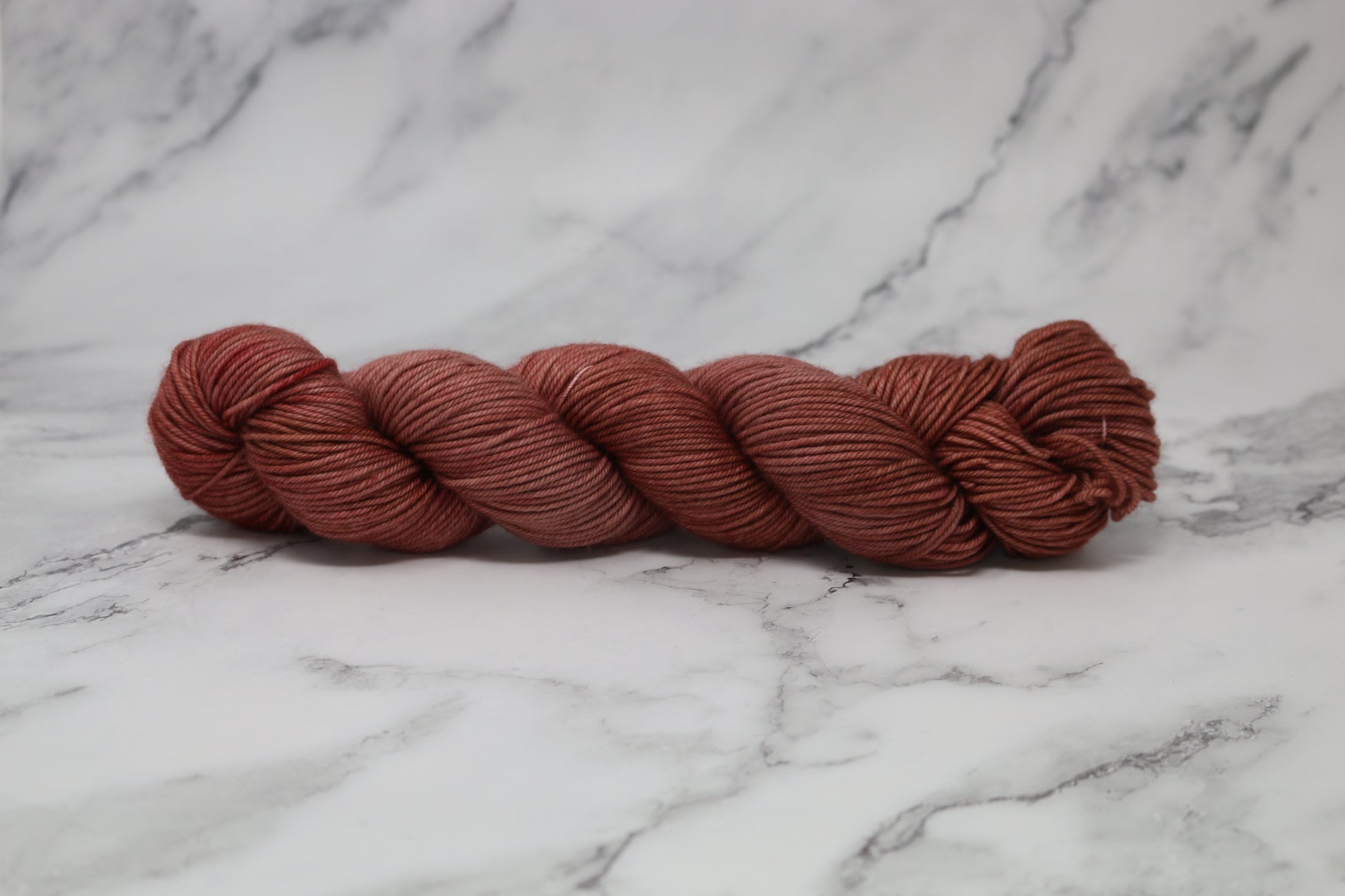 A skein of tonal red/brown yarn on a white marble surface and background