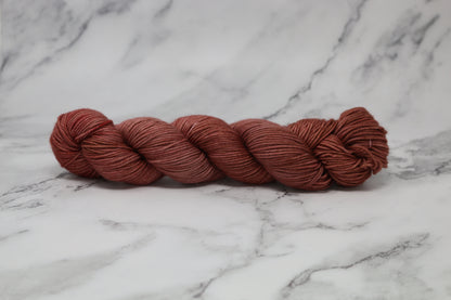 A skein of tonal red/brown yarn on a white marble surface and background