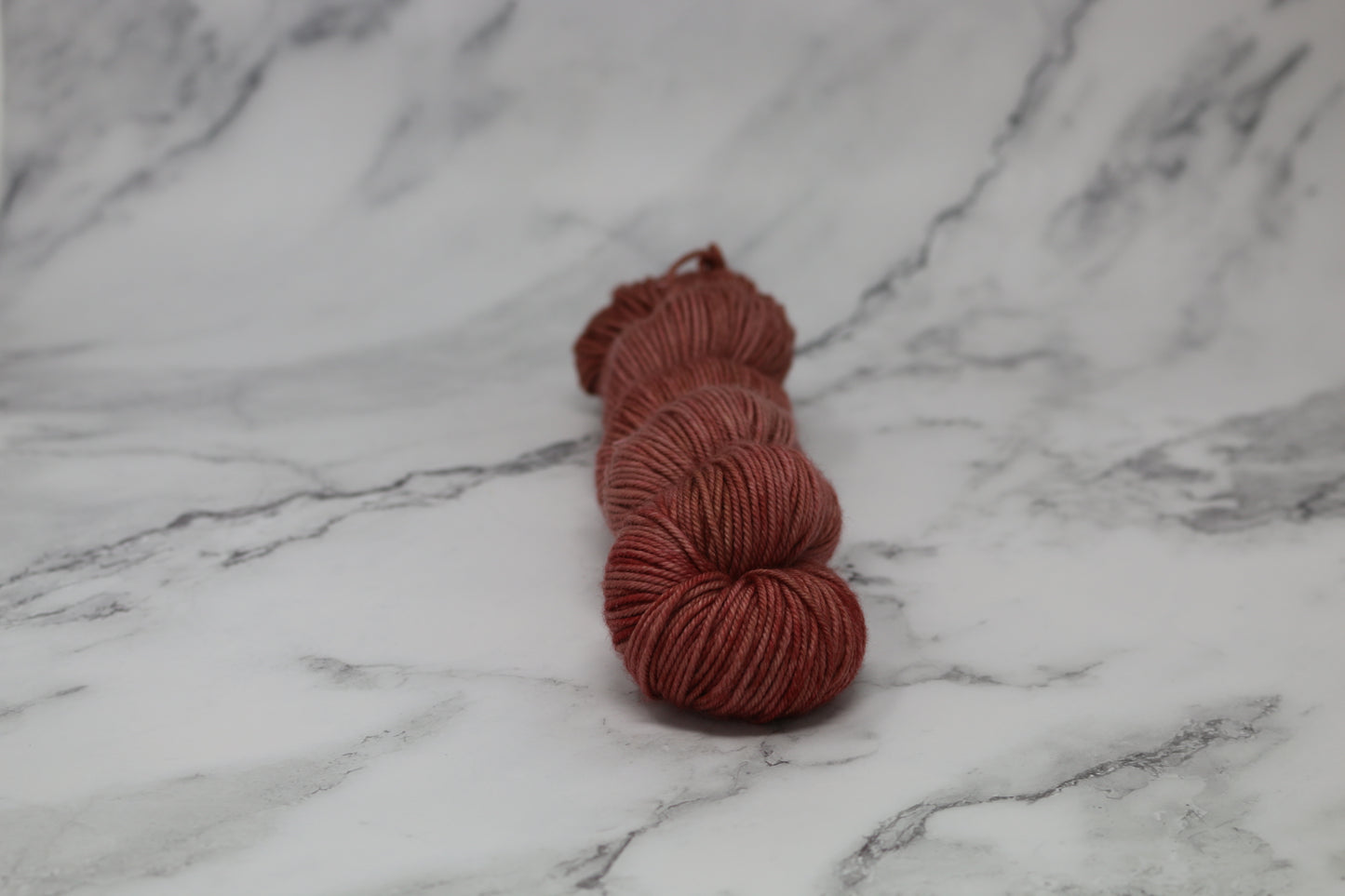 A skein of tonal red/brown yarn on a white marble surface and background