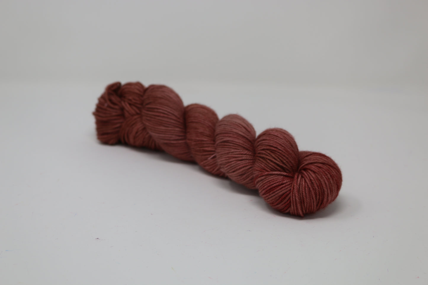 A skein of tonal red/brown yarn on a white surface and background