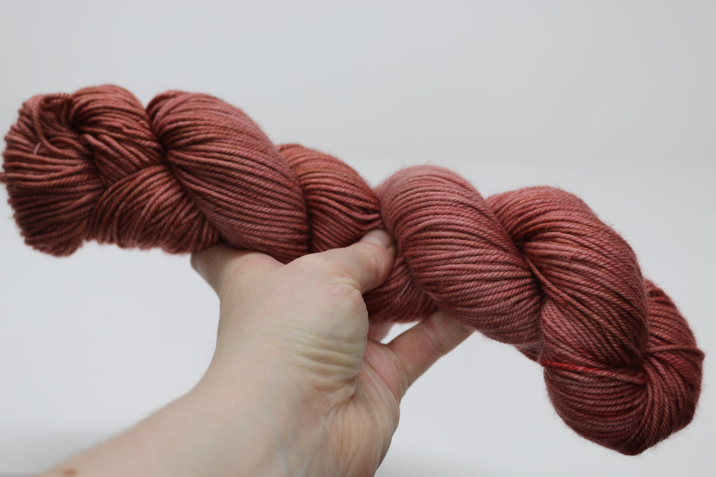 A skein of red/brown tonal yarn held in a person's left hand in front of a white background