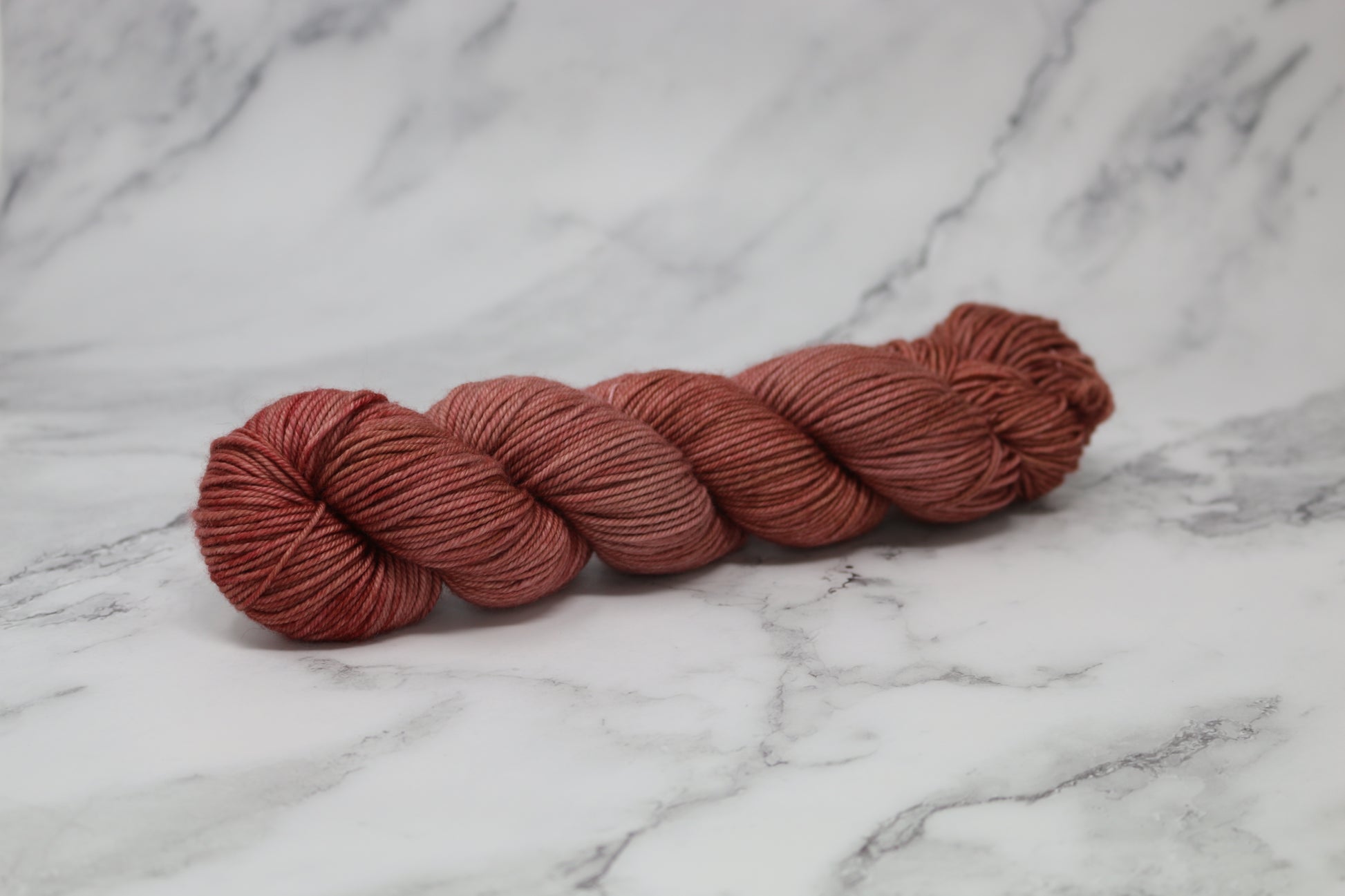 A skein of tonal red/brown yarn on a white marble surface and background