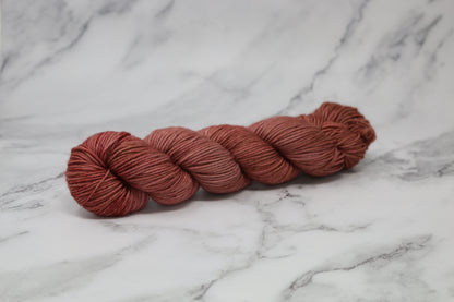 A skein of tonal red/brown yarn on a white marble surface and background