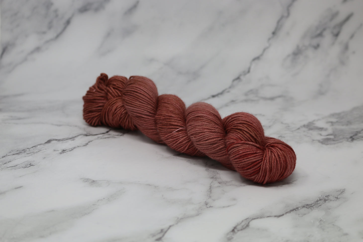 A skein of tonal red/brown yarn on a white marble surface and background