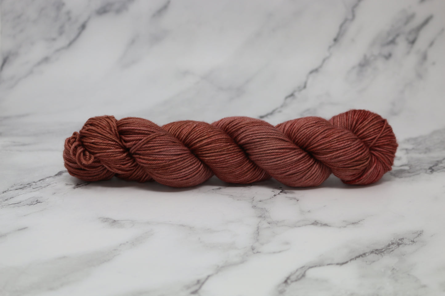 A skein of tonal red/brown yarn on a white marble surface and background
