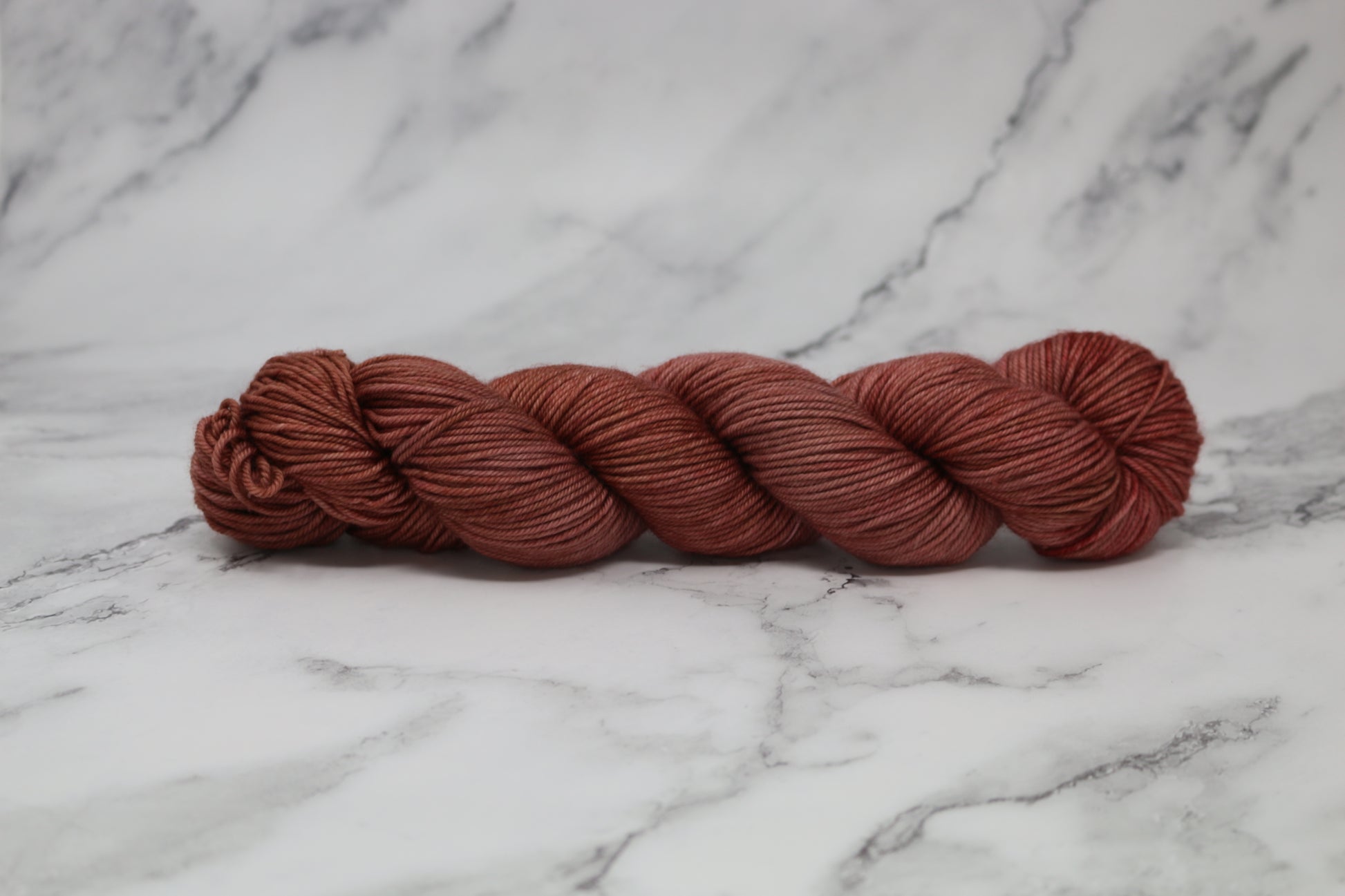 A skein of tonal red/brown yarn on a white marble surface and background