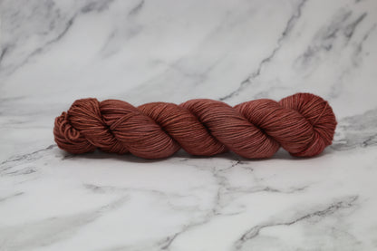 A skein of tonal red/brown yarn on a white marble surface and background