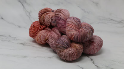 Three skeins of yarn in dusty rose, mauve, and terracotta tones