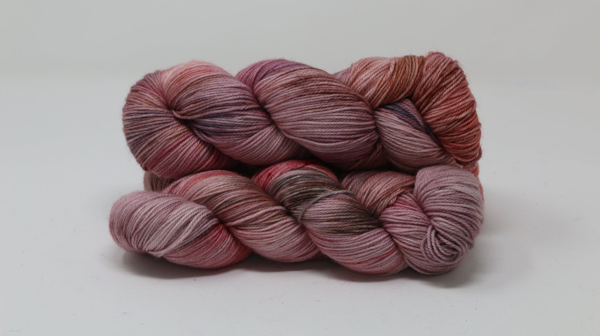 Three skeins of yarn in dusty rose, mauve, and terracotta tones