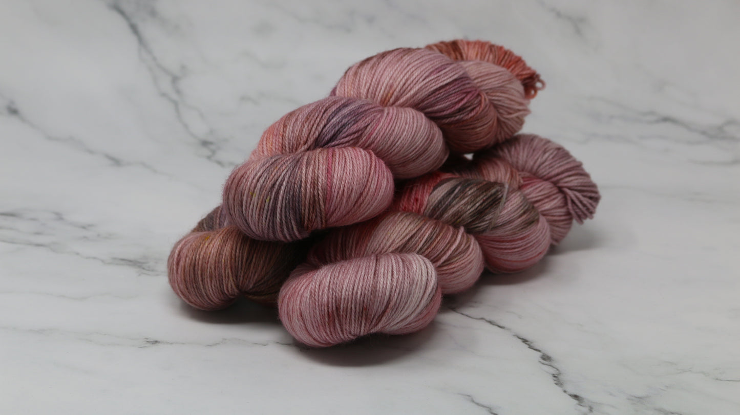 Three skeins of yarn in dusty rose, mauve, and terracotta tones