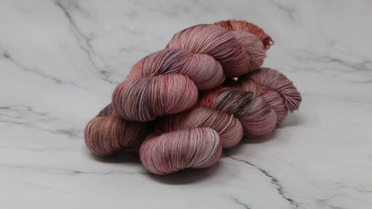 Three skeins of yarn in dusty rose, mauve, and terracotta tones