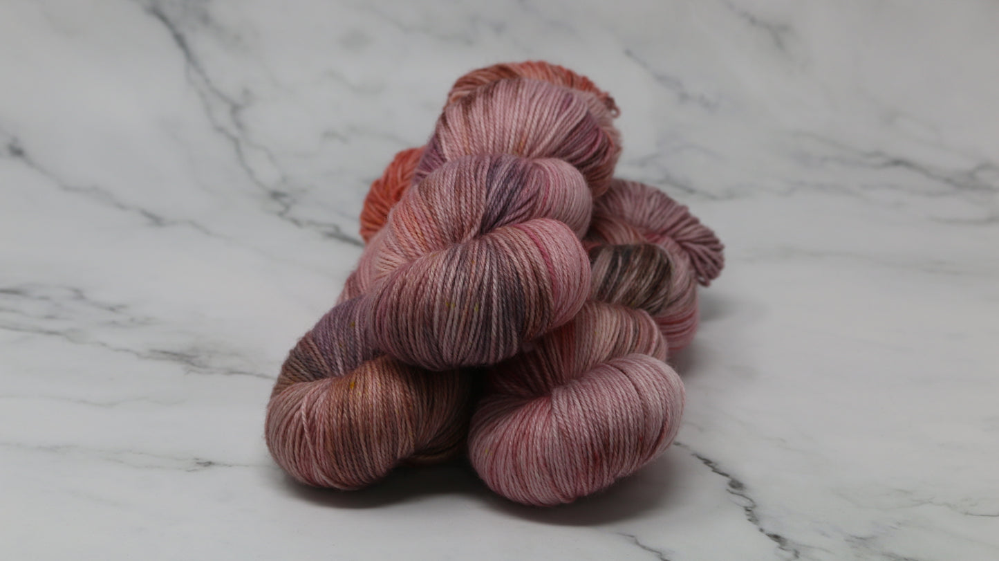 Three skeins of yarn in dusty rose, mauve, and terracotta tones