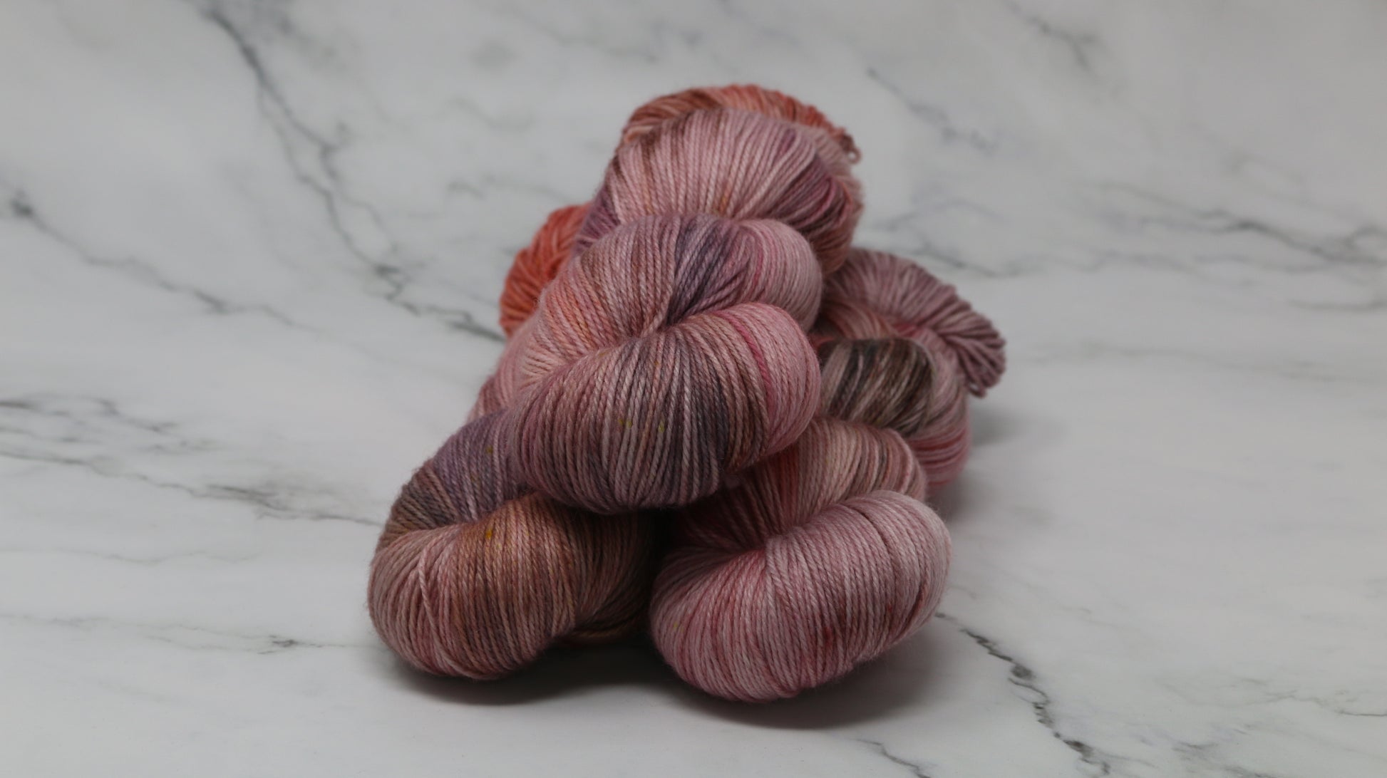 Three skeins of yarn in dusty rose, mauve, and terracotta tones