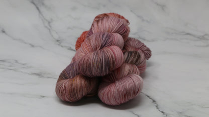 Three skeins of yarn in dusty rose, mauve, and terracotta tones