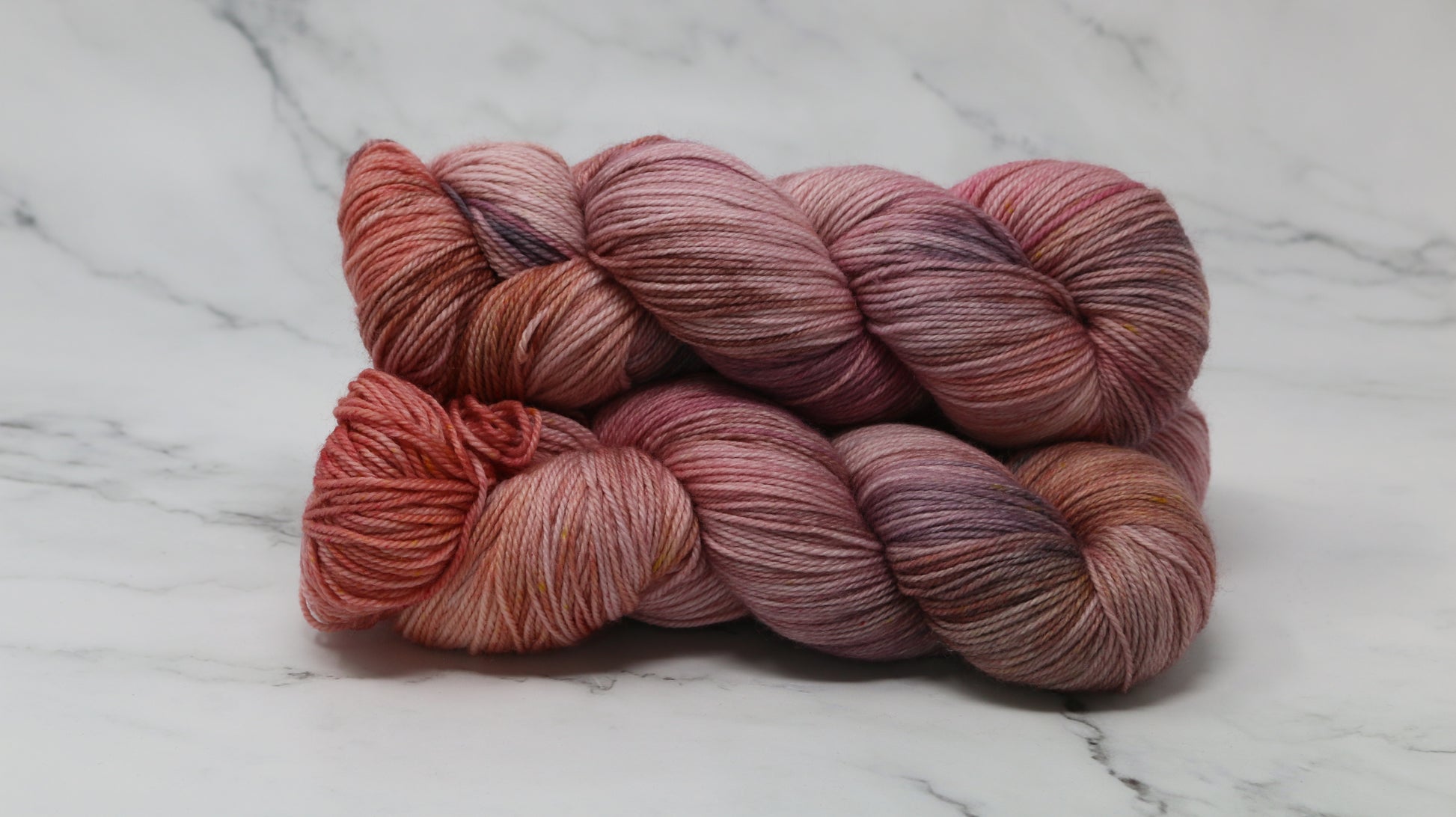 Three skeins of yarn in dusty rose, mauve, and terracotta tones