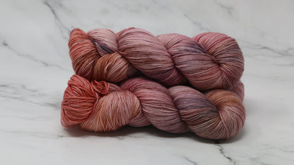 Three skeins of yarn in dusty rose, mauve, and terracotta tones