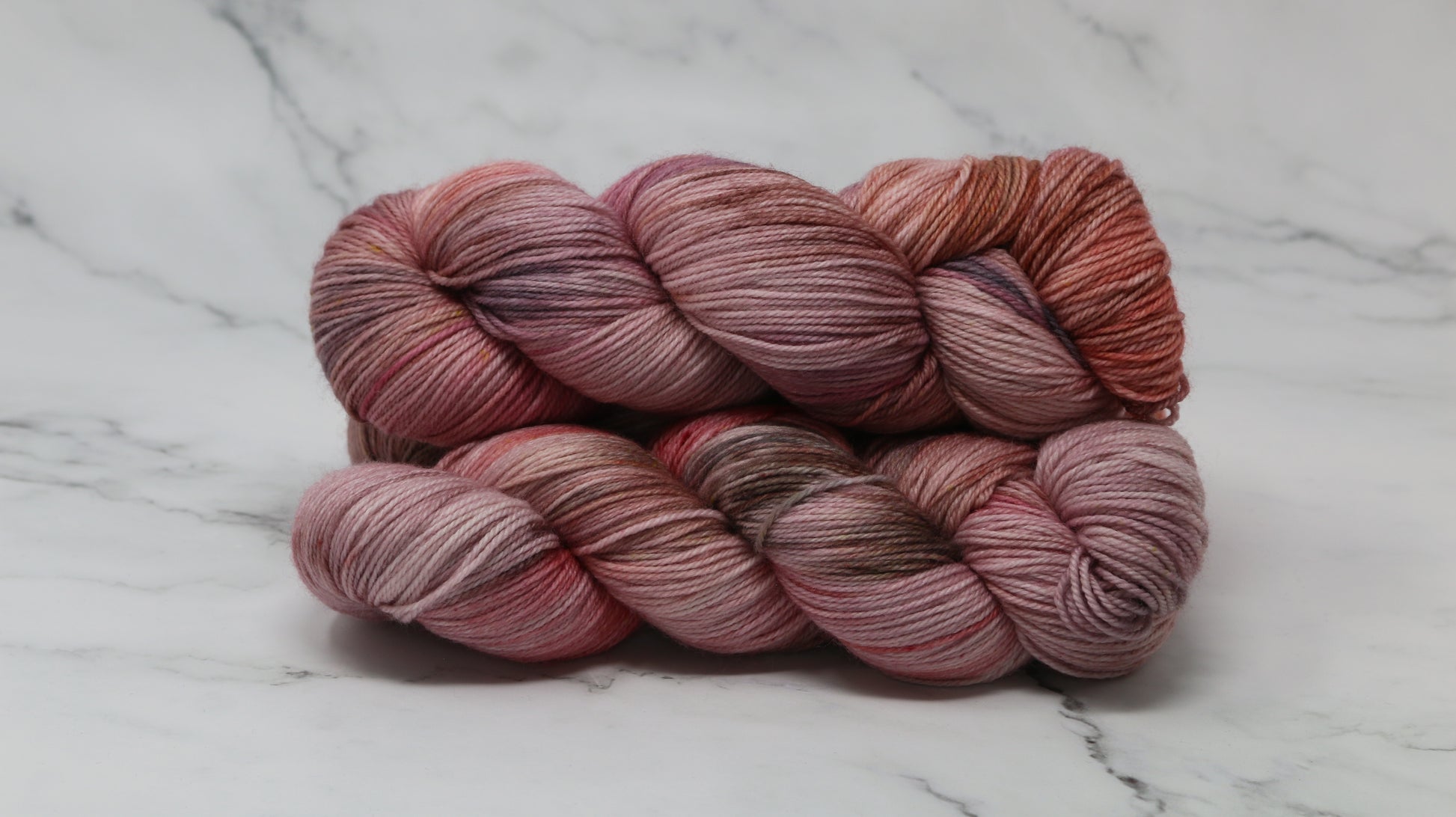 Three skeins of yarn in dusty rose, mauve, and terracotta tones