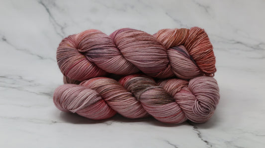 Three skeins of yarn in dusty rose, mauve, and terracotta tones