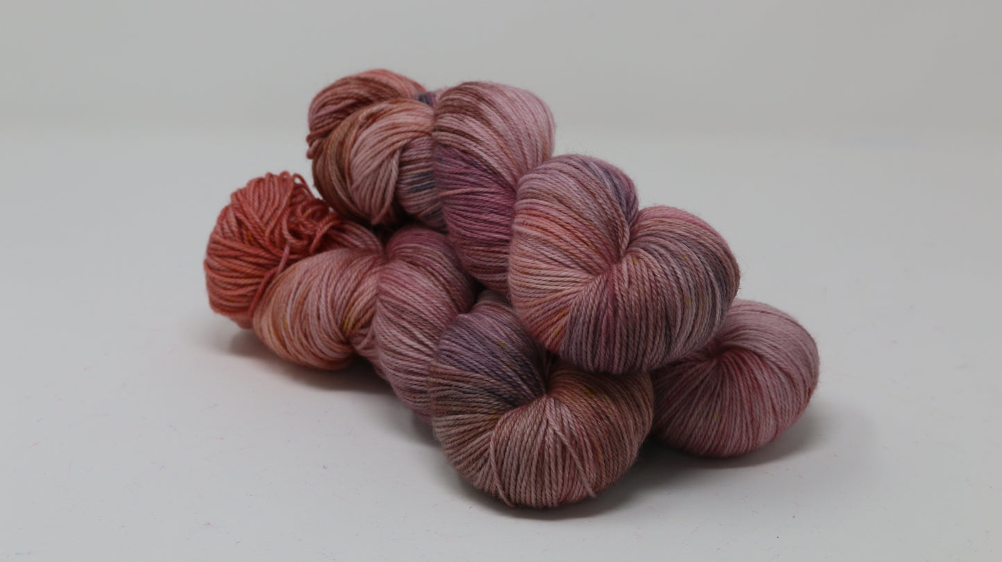 Three skeins of yarn in dusty rose, mauve, and terracotta tones