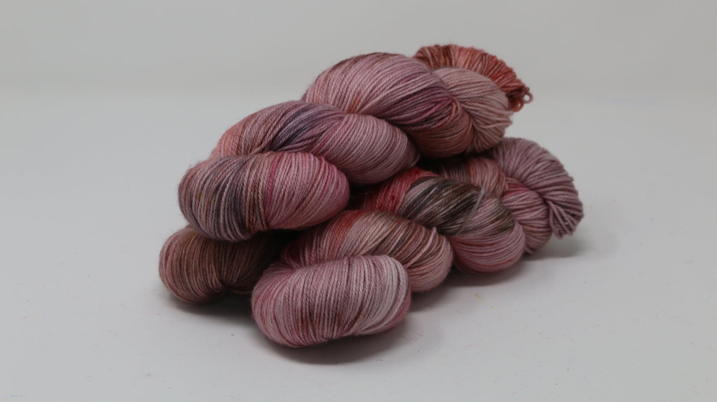 Three skeins of yarn in dusty rose, mauve, and terracotta tones