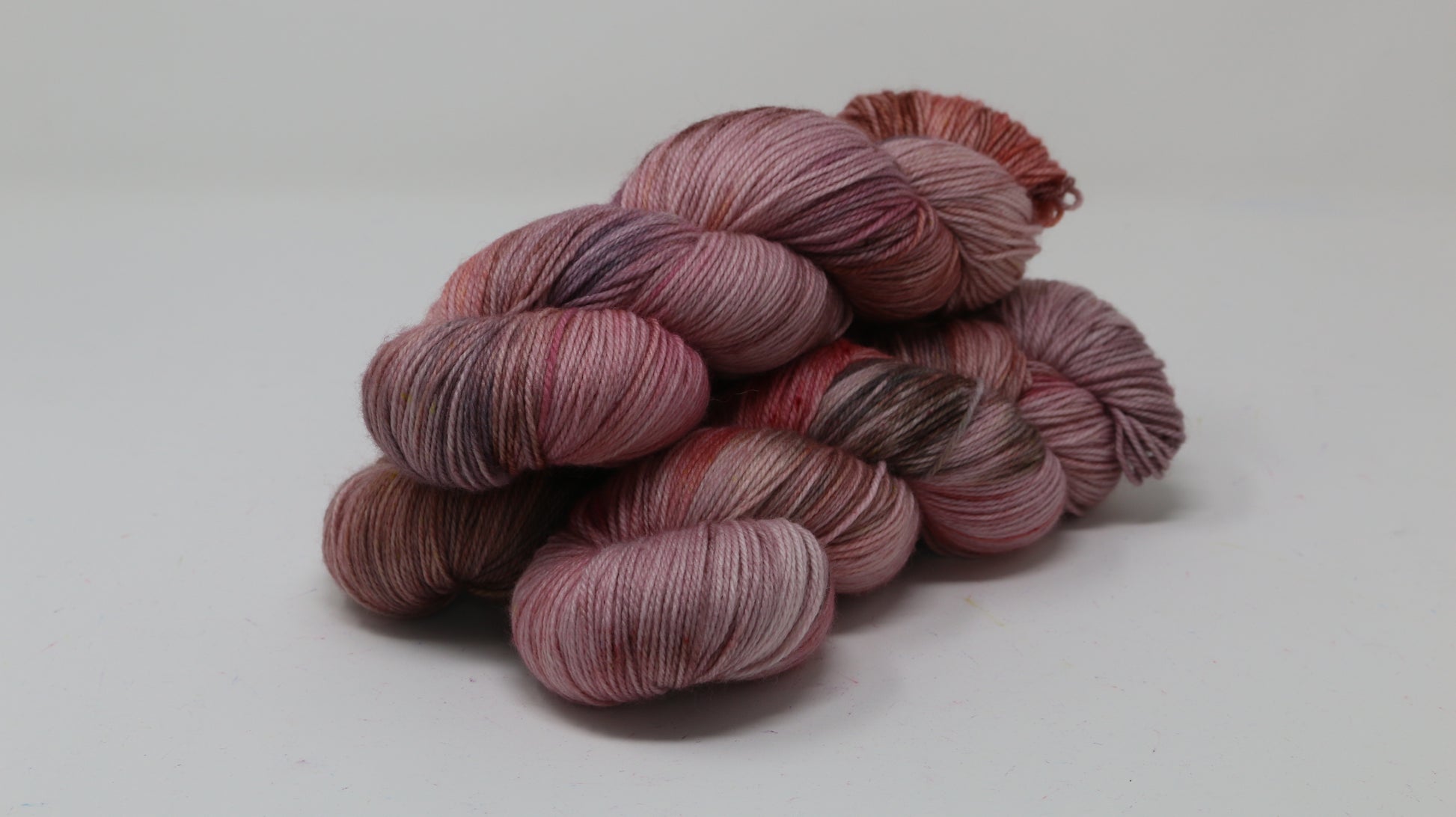 Three skeins of yarn in dusty rose, mauve, and terracotta tones