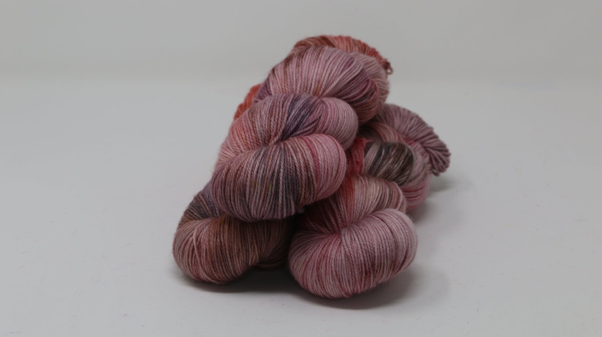 Three skeins of yarn in dusty rose, mauve, and terracotta tones
