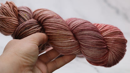 A skein of pink variegated yarn held in a person's left hand in front of a white background