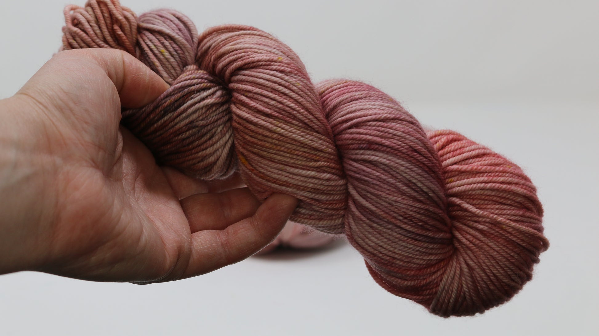 A skein of pink variegated yarn held in a person's left hand in front of a white background