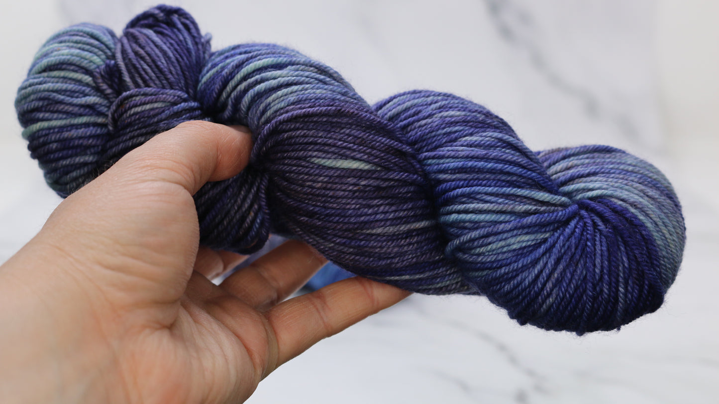 A skein of blue variegated yarn held in a person's left hand in front of a white background
