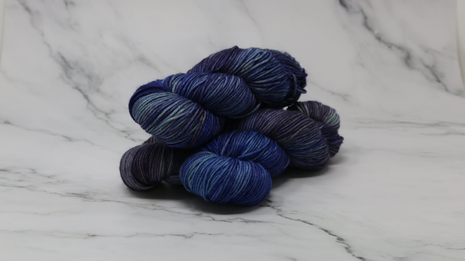 3 skeins of blue variegated yarn on a white marble background and surface