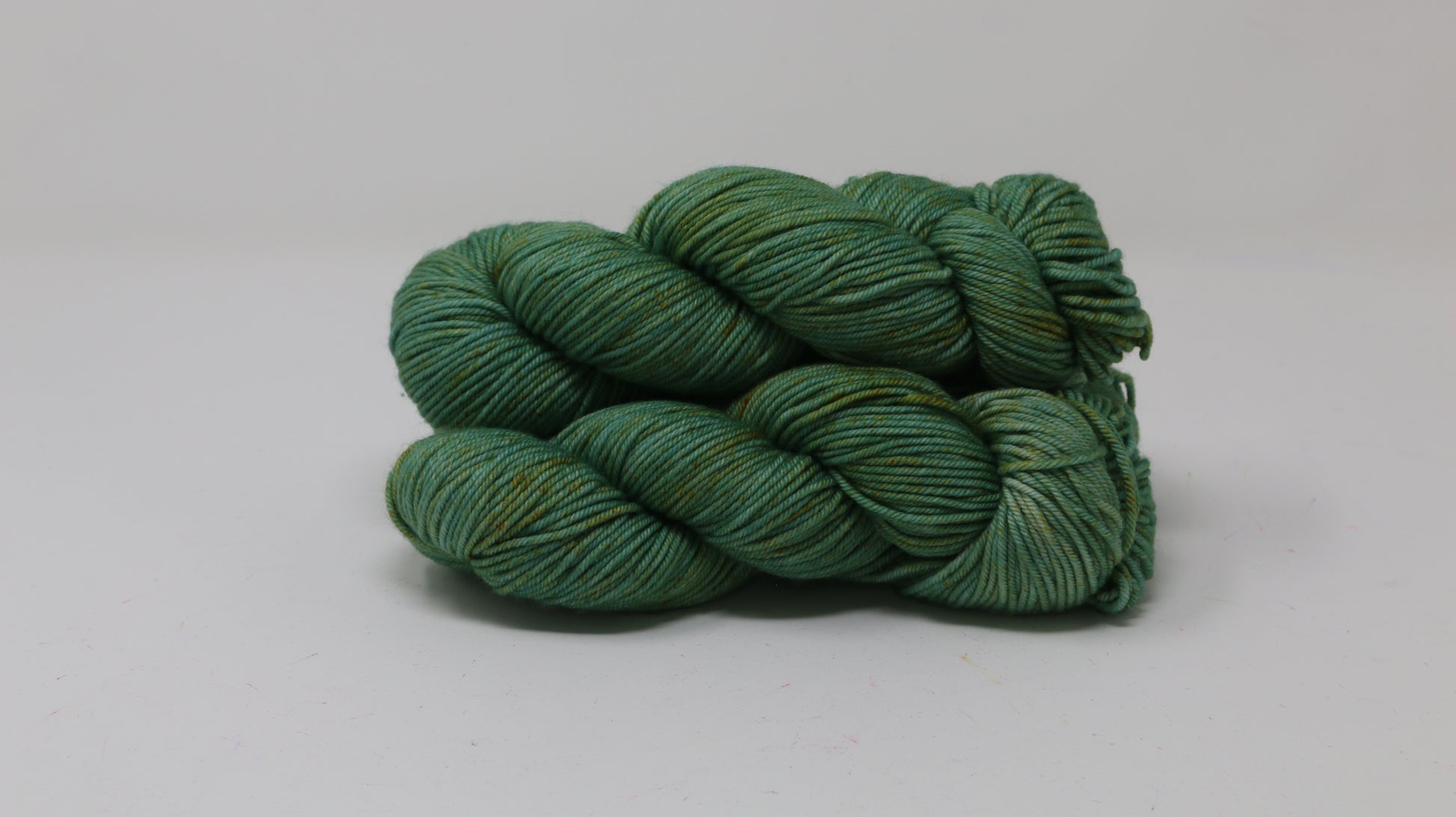 3 skeins of green yarn speckled with gold accents displayed on a white surface and background