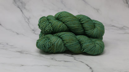 3 skeins of green yarn speckled with gold accents displayed on a white marble surface and background