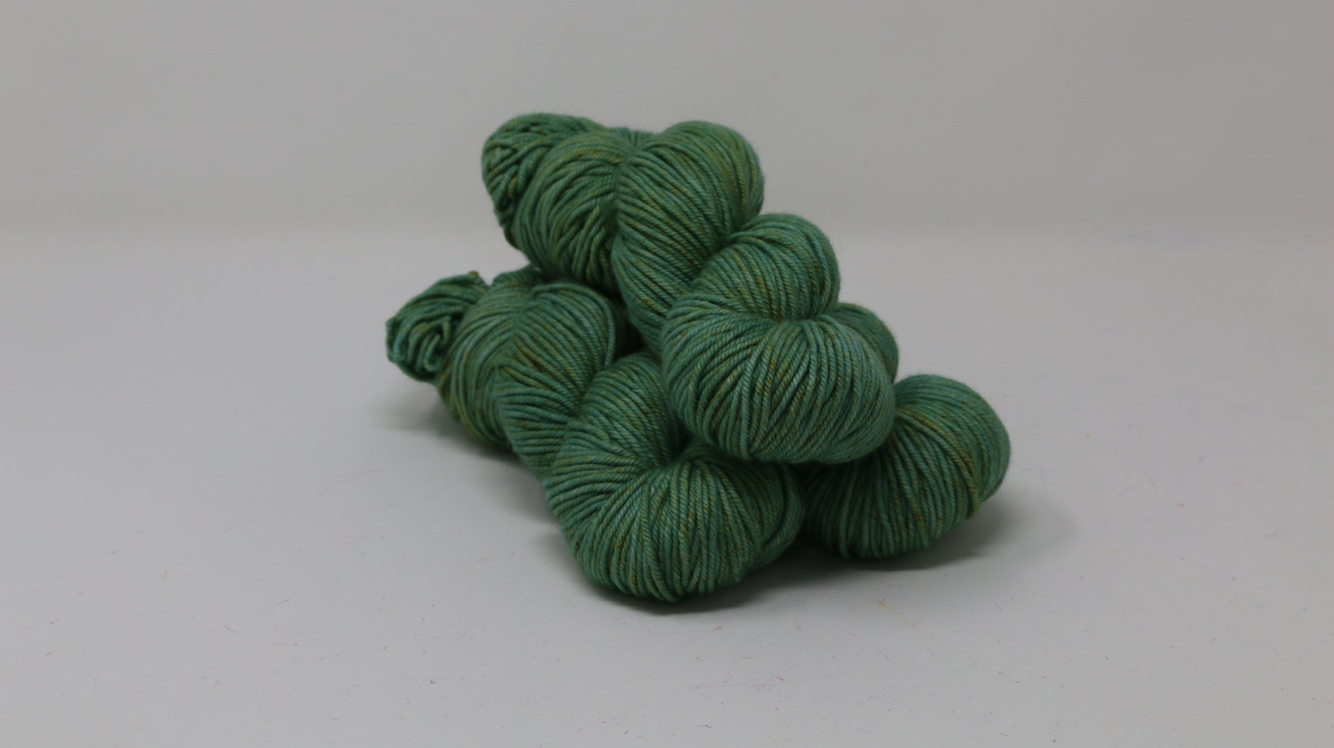 3 skeins of green yarn speckled with gold accents displayed on a white surface and background
