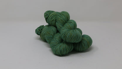 3 skeins of green yarn speckled with gold accents displayed on a white surface and background