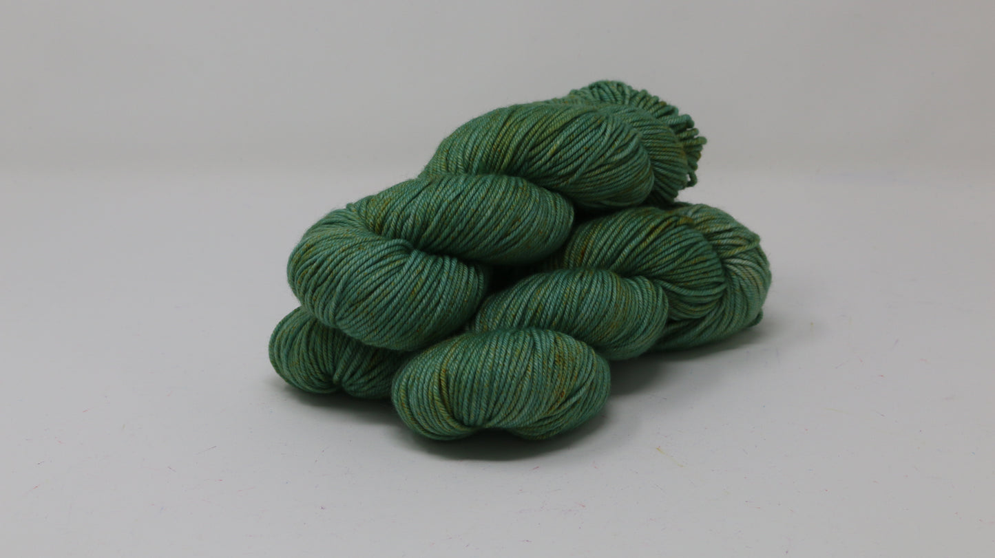 3 skeins of green yarn speckled with gold accents displayed on a white surface and background