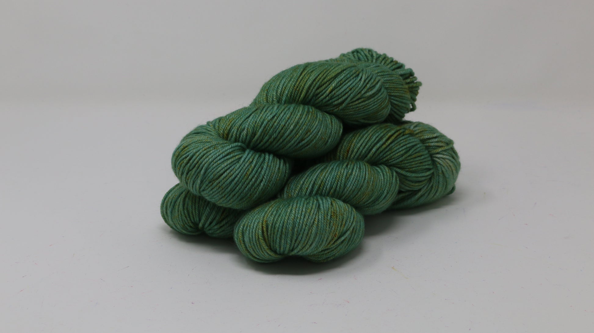 3 skeins of green yarn speckled with gold accents displayed on a white surface and background