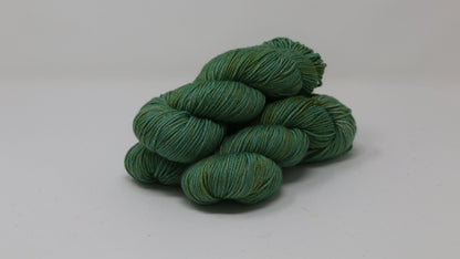 3 skeins of green yarn speckled with gold accents displayed on a white surface and background