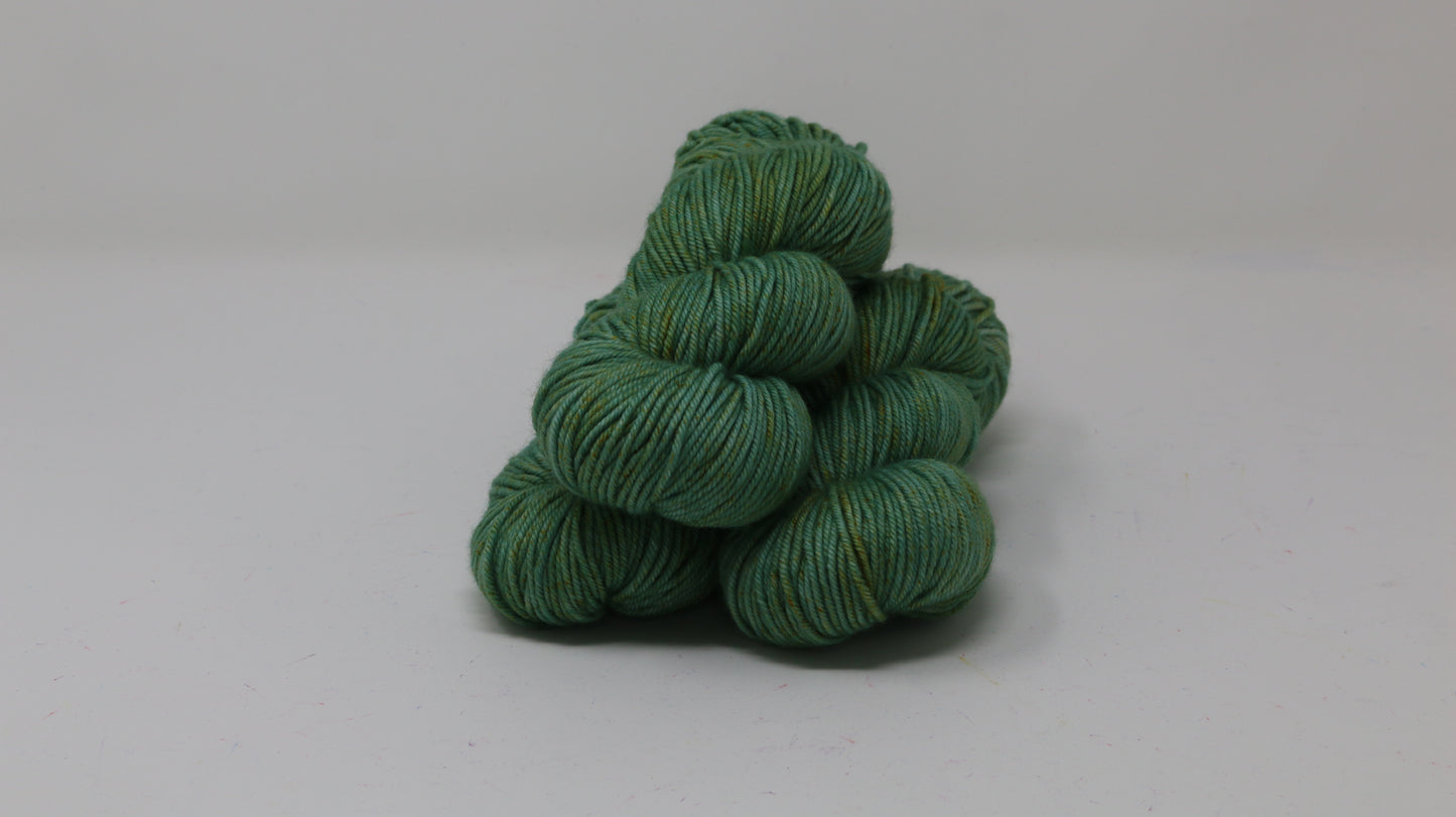 3 skeins of green yarn speckled with gold accents displayed on a white surface and background