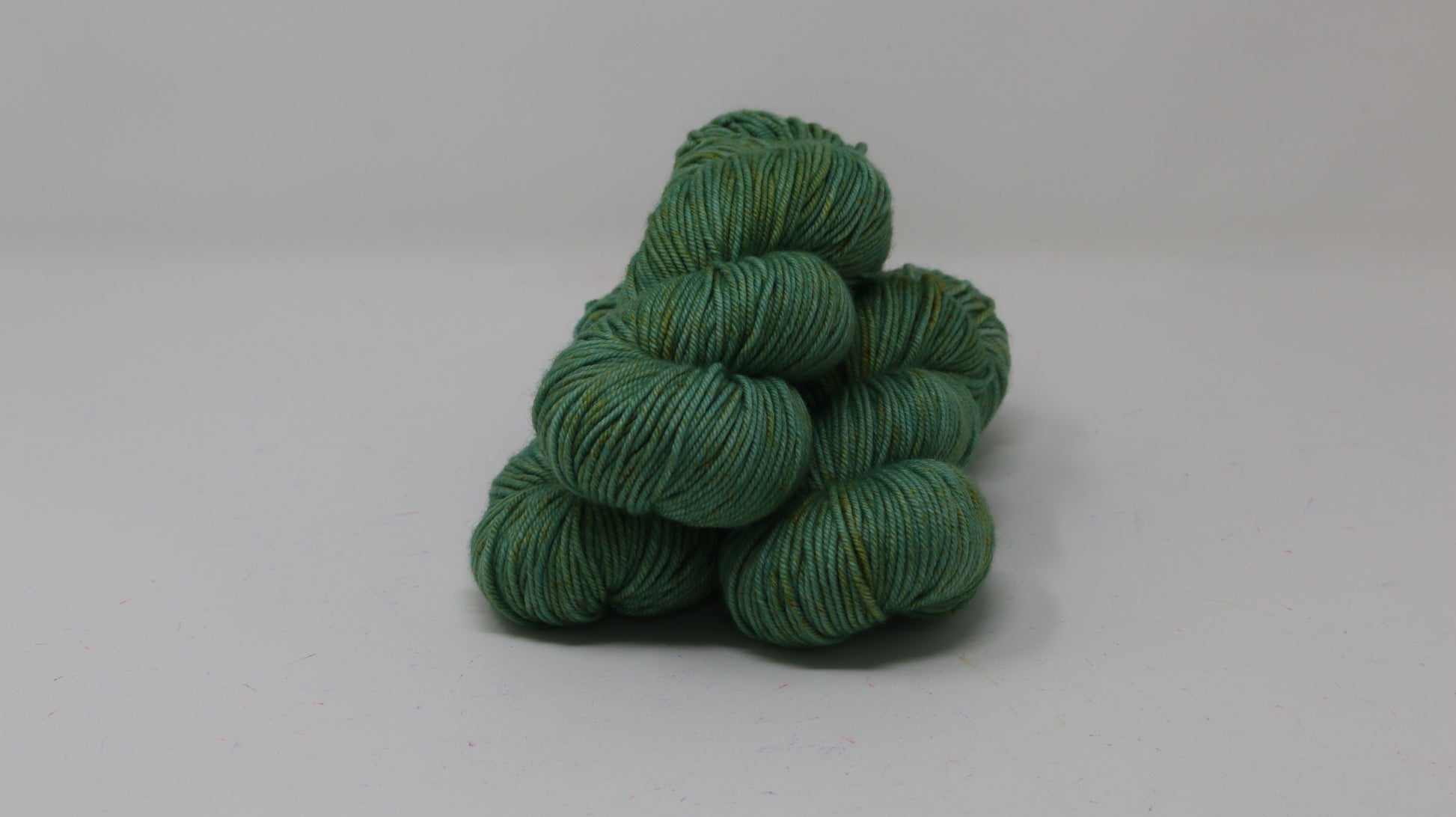 3 skeins of green yarn speckled with gold accents displayed on a white surface and background