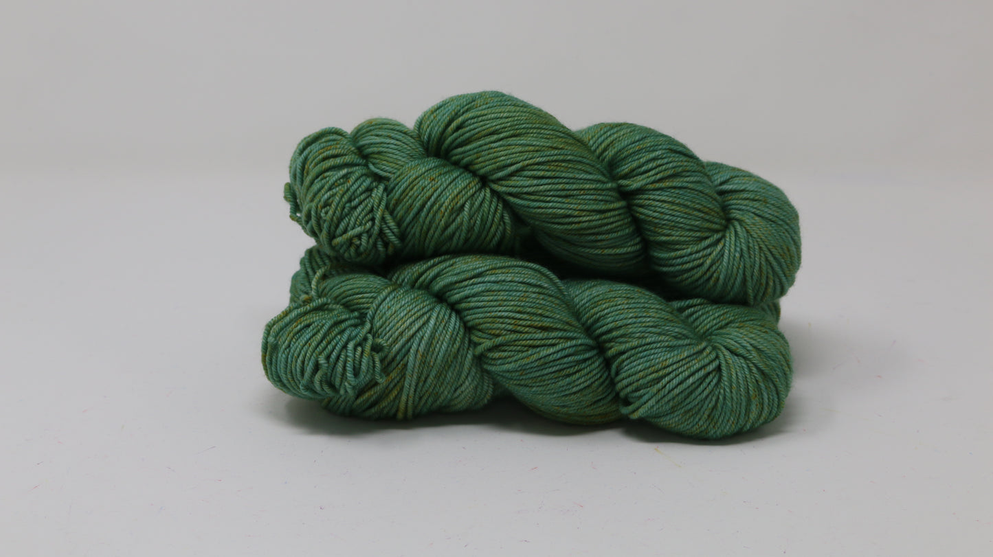 3 skeins of green yarn speckled with gold accents displayed on a white surface and background