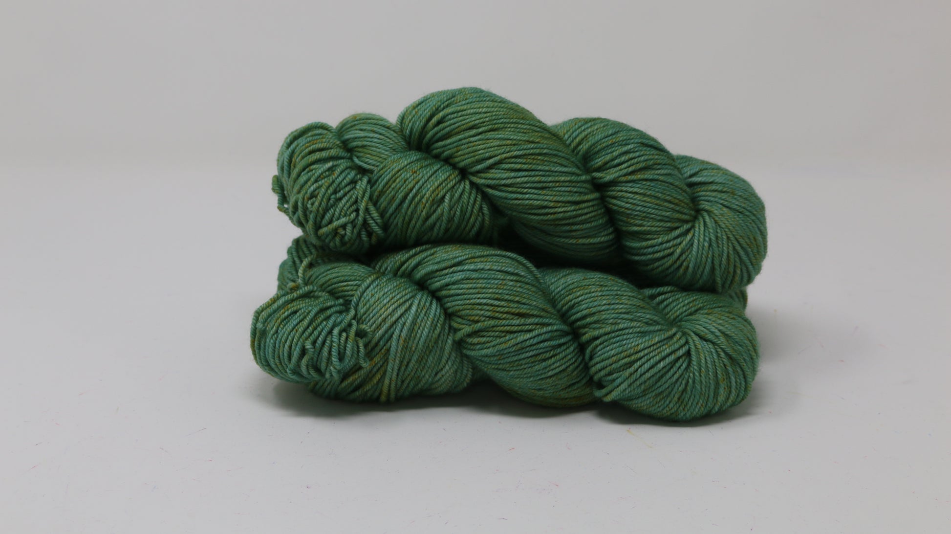 3 skeins of green yarn speckled with gold accents displayed on a white surface and background