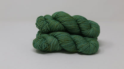 3 skeins of green yarn speckled with gold accents displayed on a white surface and background